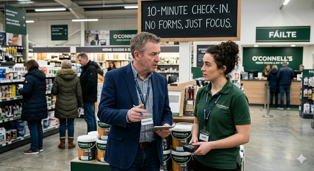 A manager and team member in a brief shopfloor conversation — the ten-minute check-in replacing the annual review